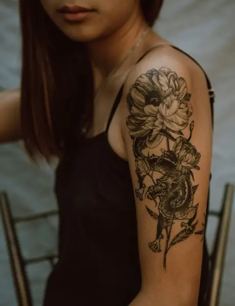 Black-and-grey peony and dragon tattoo on an upper arm