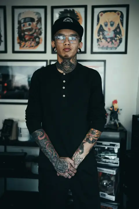 Tattooed artist standing in his studio in front of framed flash